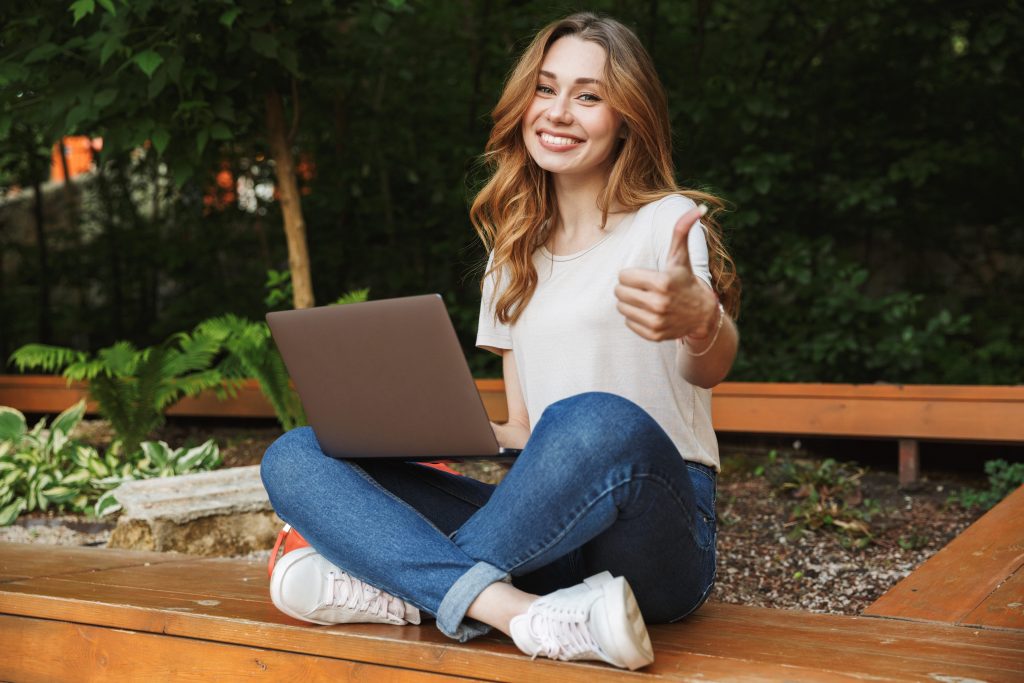 avanco-da-tecnologia-mulher-jovem-sentada-computador-feliz-fazendo-joinha