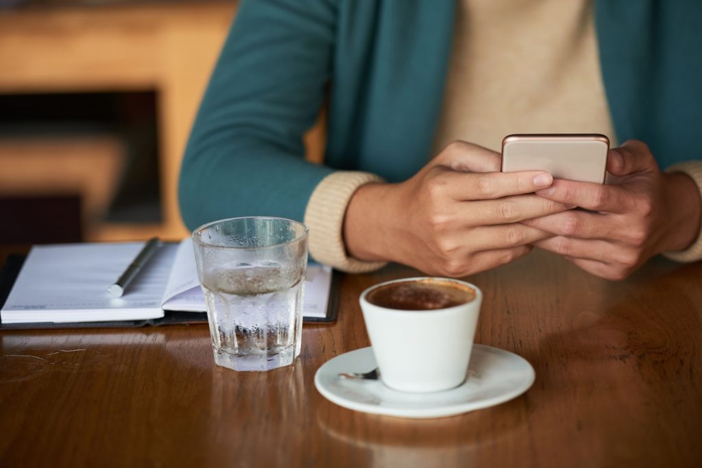 mulher-tomando-café-anotando-na-agenda-e-mexendo-no-celular